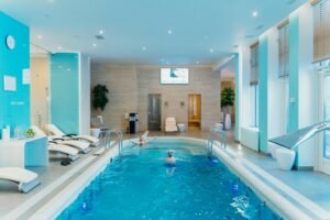 Luxurious indoor swimming pool in a modern spa with lounge chairs and soft lighting.